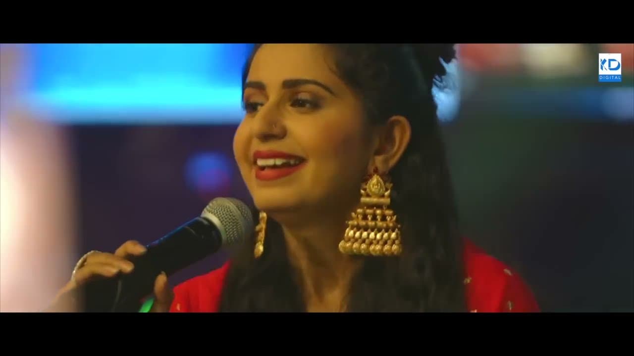 Kinjal Dave singing into a microphone, lit in warm stage colours