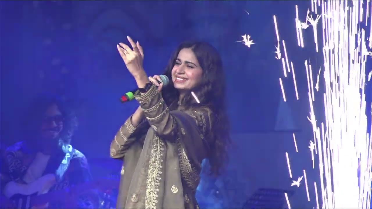 Kinjal Dave singing with her arm raised as sparks fall across the stage